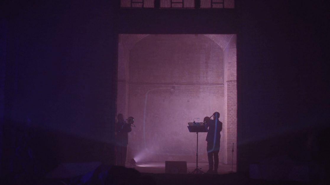 Musicians framed by soft pink light in large concrete space