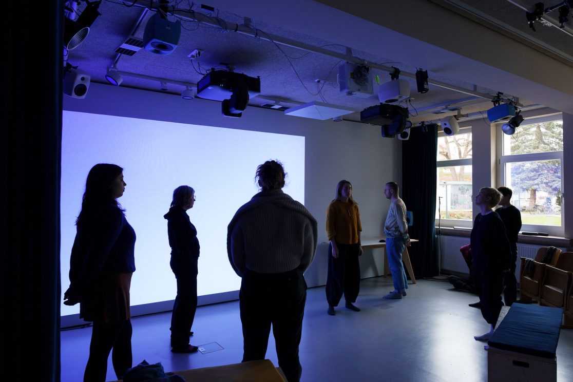 group of people standing still in a workshop room with blue light from a projection