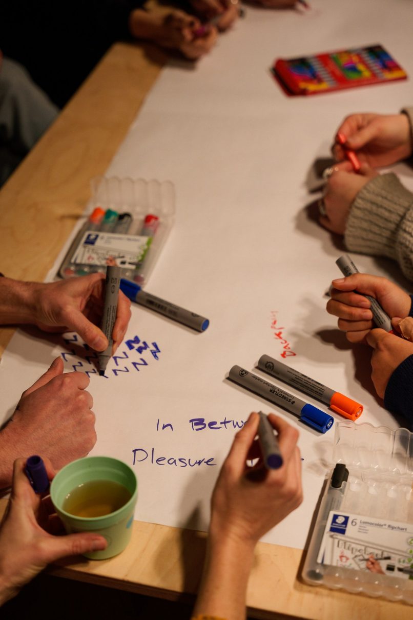 detail of a table with many hands and pens working together on a large sheet of paper
